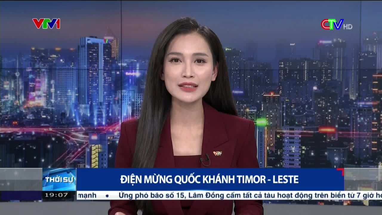 A woman in a maroon blazer stands in front of a cityscape backdrop, speaking into a camera. The lower third of the screen displays Vietnamese text with a headline about Timor-Leste.
A woman in a maroon blazer stands in front of a cityscape backdrop, speaking into a camera. The lower third of the screen displays Vietnamese text with a headline about Timor-Leste.