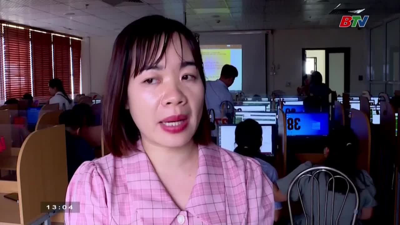 A woman in a pink plaid shirt speaks directly to the camera, likely for Bac Ninh TV. Behind her, students sit at computers in a classroom, illuminated by the glow of their screens.
