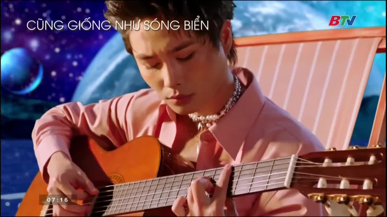 A man in a pink shirt strums a guitar, his fingers moving across the frets. The scene is on Bac Ninh TV, with a backdrop of a galaxy and the words "Cũng Giống Như Sóng Biển" above.
