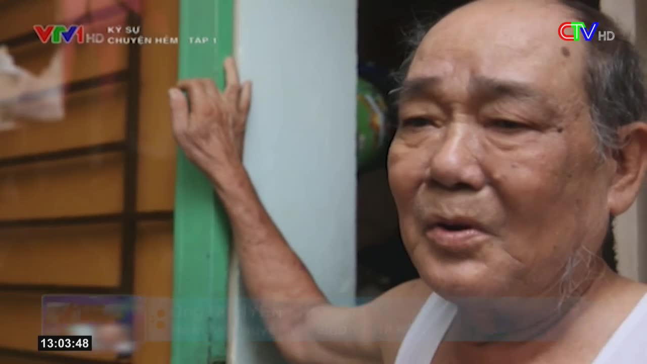 An older man, wearing a white tank top, speaks directly to the camera, his hand resting on a green door frame. The Ca Mau TV logo is visible in the corner, and the episode title is "Kỹ Sư Chuyện Hẻm."
