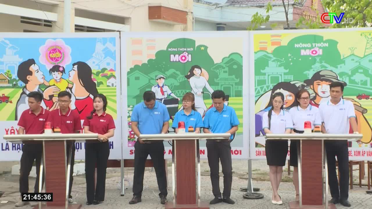 Teams of people stand behind podiums, facing the camera, with large, colorful posters behind them. A red light sits atop each podium, ready for a quick push.
