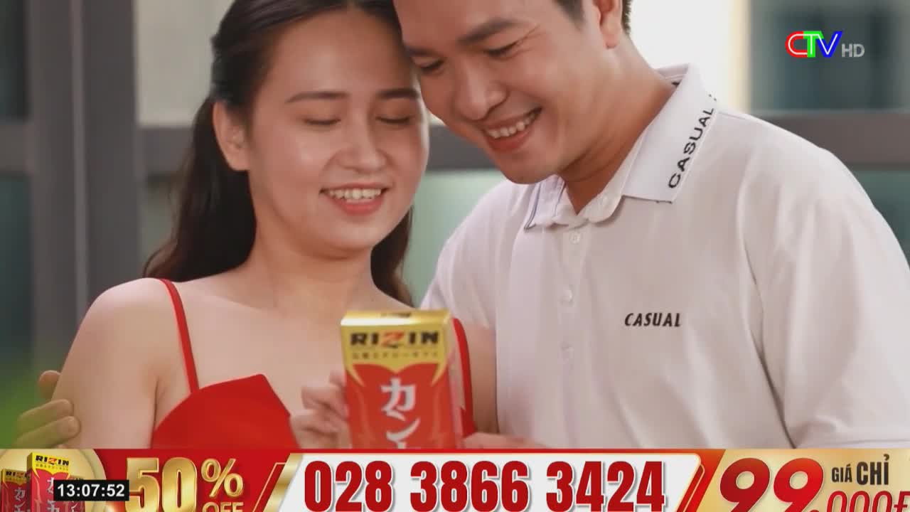 A smiling couple is holding a small, red and gold box, looking at it with delight. The Ca Mau TV logo is in the corner, and a phone number and discount are displayed at the bottom of the screen.
