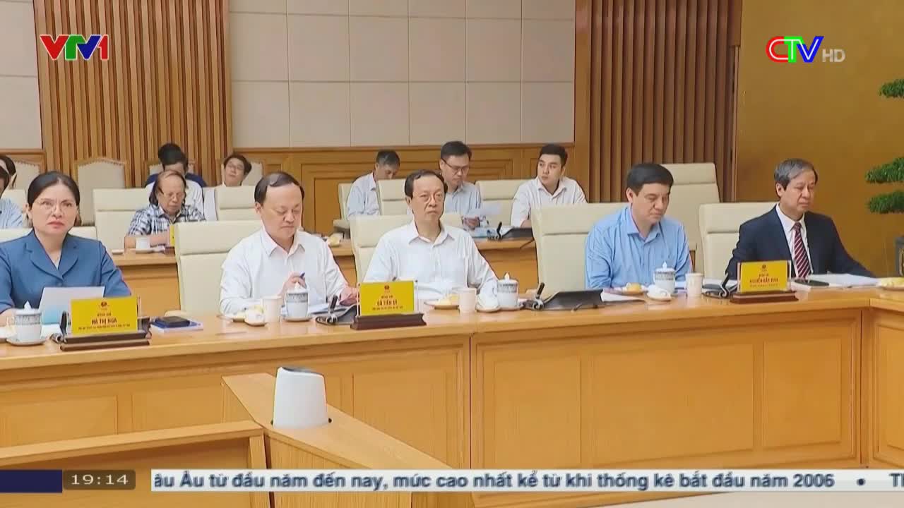 A meeting is underway, with people seated at a long table, their nameplates in front of them. The Ca Mau TV logo is in the corner, and a news ticker scrolls across the bottom of the screen.
