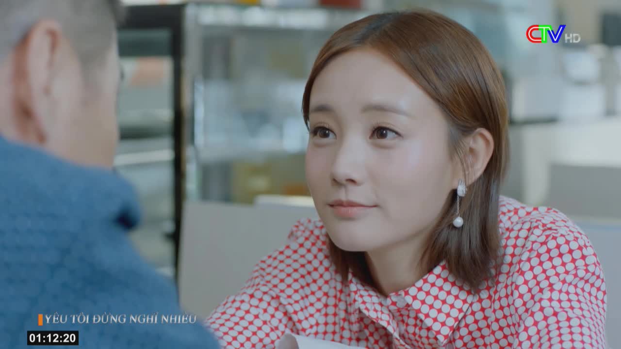 A woman with pearl earrings and a red and white polka-dot shirt looks intently at someone off-screen. The Ca Mau TV logo is visible in the corner, and the timecode shows 01:12:20.
