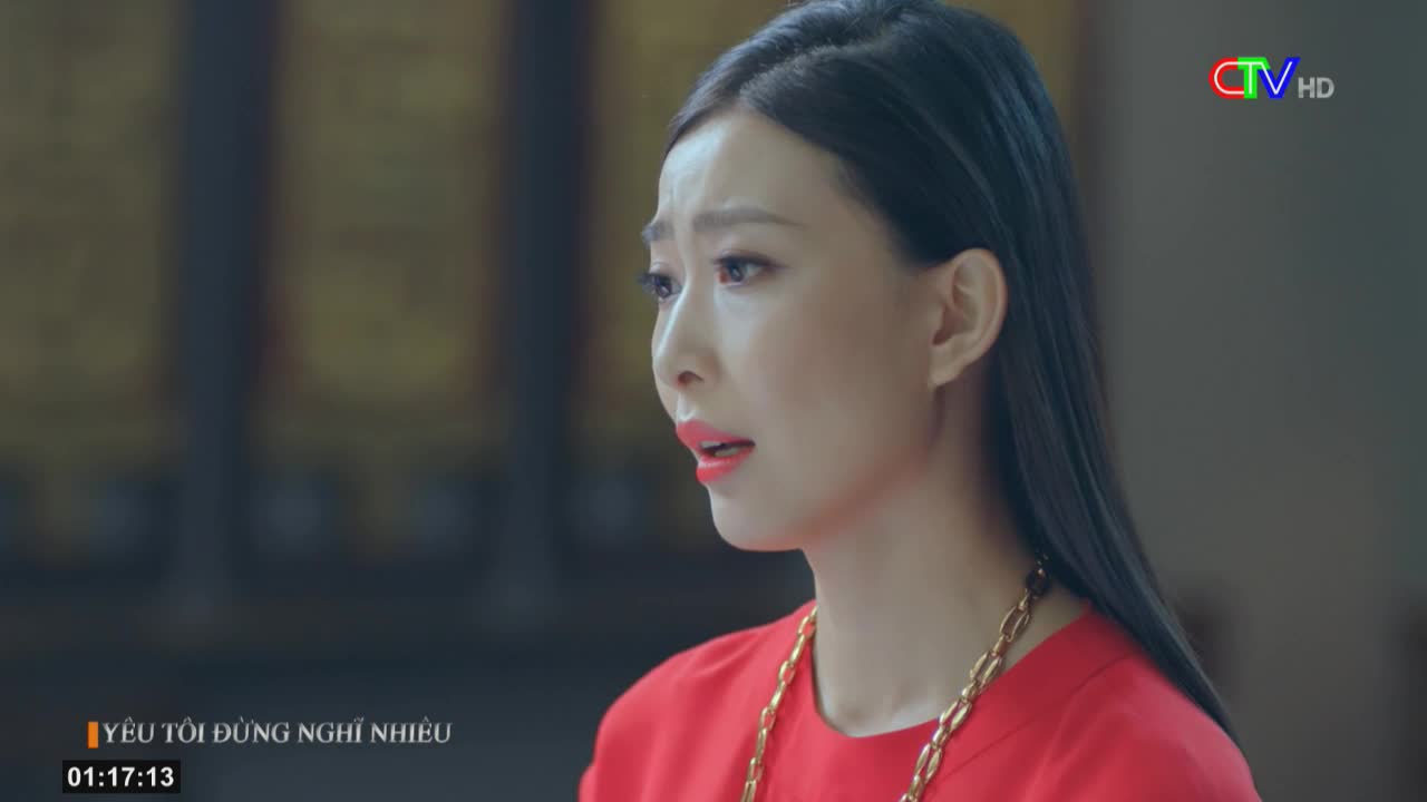 A woman in a red top, with a gold chain, looks off to the side with a pained expression. The Ca Mau TV logo is visible in the corner, and the subtitles indicate a Vietnamese drama is playing.
