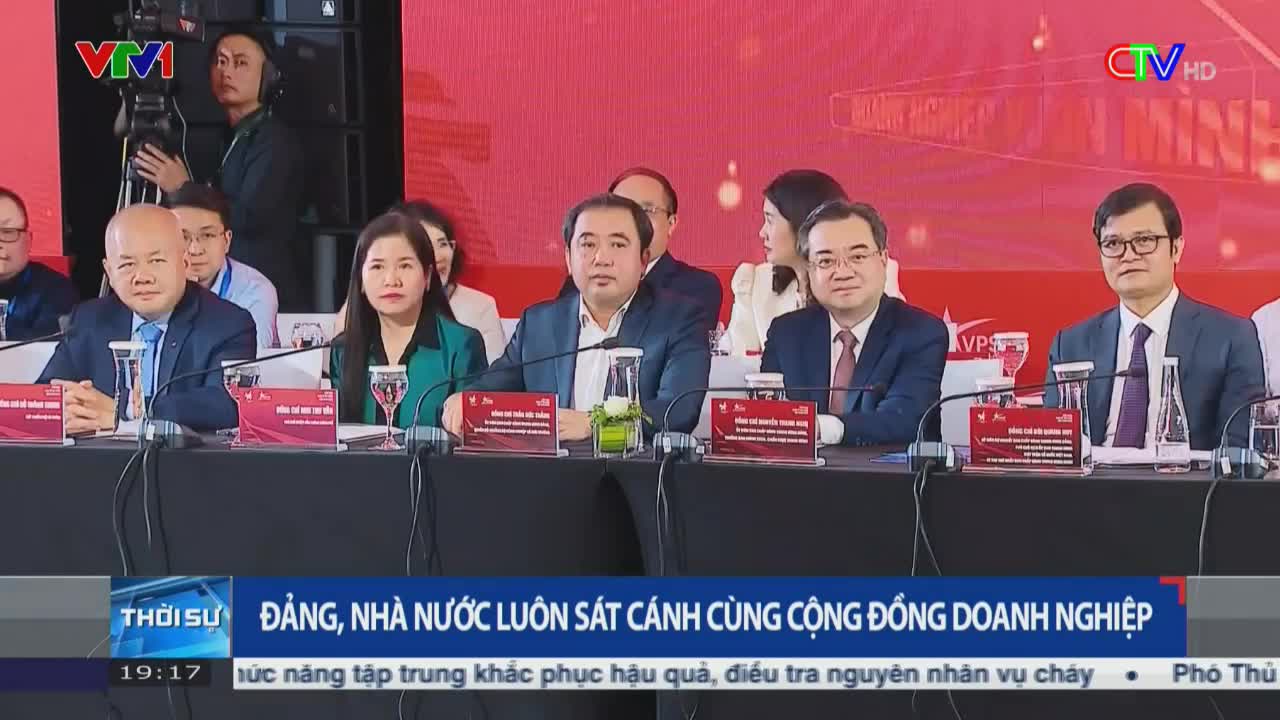 A panel of suited individuals sits at a long table, facing forward under bright lights. The Ca Mau TV logo is visible in the corner, and the bottom of the screen displays Vietnamese text.
