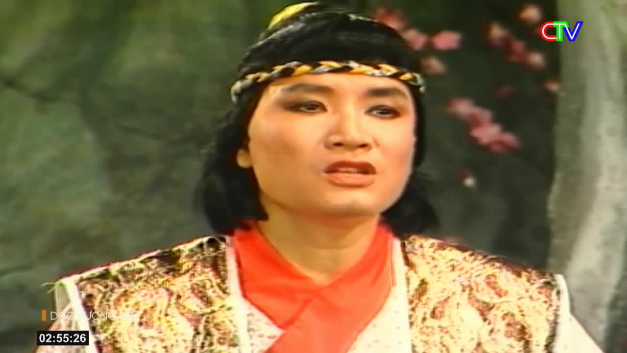 A performer in a patterned vest and orange scarf speaks with a concerned expression. The Ca Mau TV logo appears in the upper right corner.