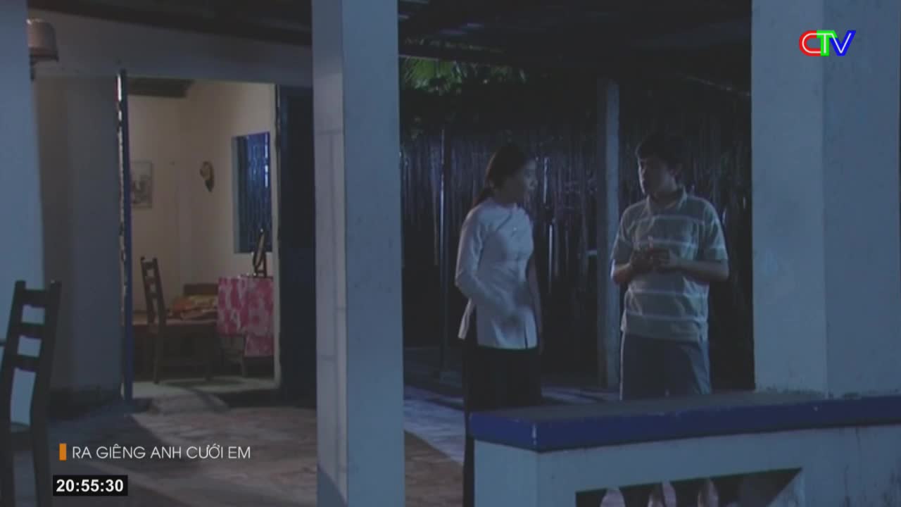 A woman in a white ao dai and a man in a striped shirt stand outside a home at night. The Ca Mau TV logo is visible in the upper right corner.