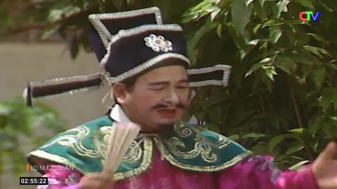A performer in a tall, ornate hat and a vibrant pink robe gestures with a fan. The Ca Mau TV logo appears in the corner of the screen.