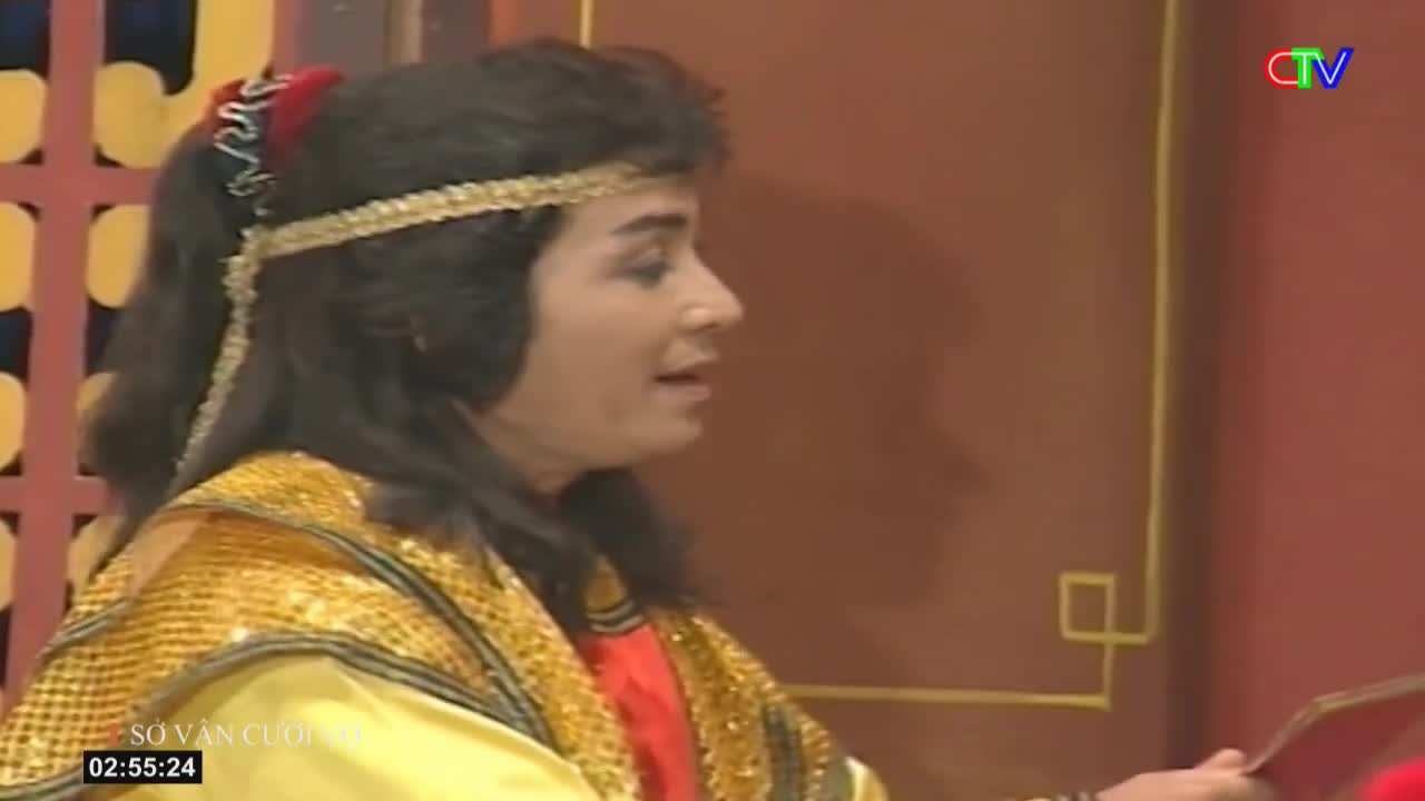 A woman in a golden costume and a jeweled headband speaks, her face turned slightly away. The Ca Mau TV logo appears in the upper right corner.