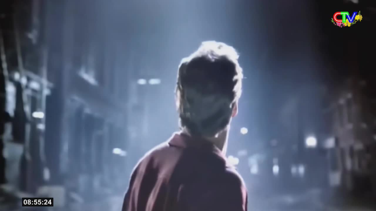 A young man stands bathed in light, his back to me, looking out at a dimly lit street. The Ca Mau TV logo flashes in the corner, a reminder of where this scene is broadcast.