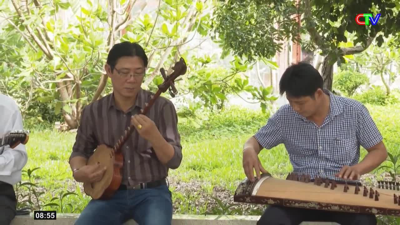 A man in a striped shirt plays a small stringed instrument, his fingers moving nimbly. Beside him, another man plucks the strings of a long, wooden zither, his head bowed in concentration.