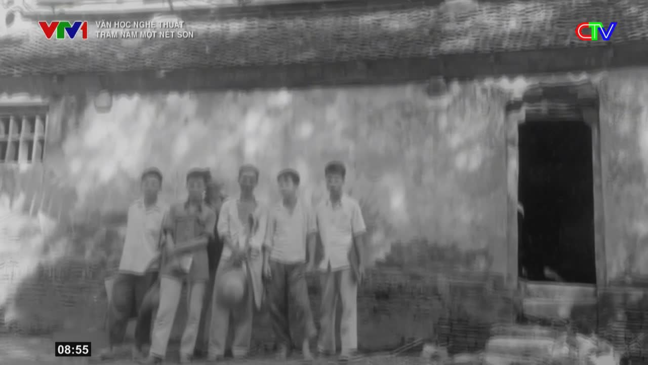 Five young men stand in front of a weathered building, their stances casual. One of them holds a round object, perhaps a hat, while another has a bag slung over his shoulder.