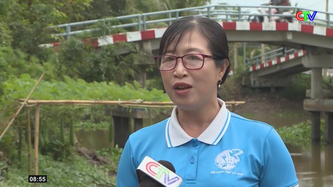 A woman in a blue shirt speaks into a CTV microphone, with a bridge and lush greenery behind her. A motorcycle passes over the bridge in the distance.