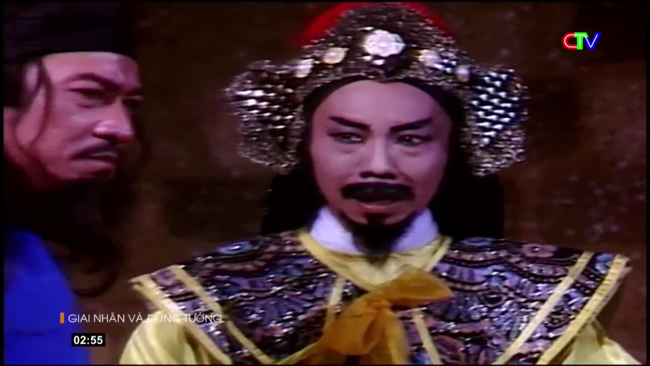 Two men in elaborate costumes stand close, one with a stern expression and dark beard, the other wearing a tall, ornate headdress. The scene is lit with a warm glow, suggesting a performance or historical reenactment.