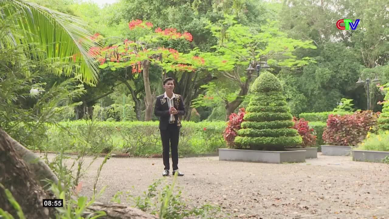 A young man stands in a manicured garden, holding two awards. The Ca Mau TV logo is visible in the upper right corner.