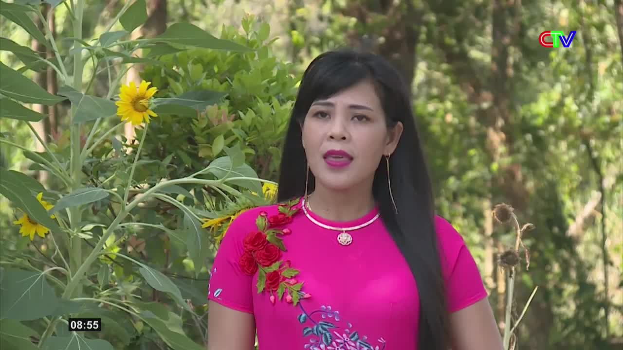 A woman in a bright pink shirt stands outdoors, with sunflowers to her left. The Ca Mau TV logo appears in the upper right corner.