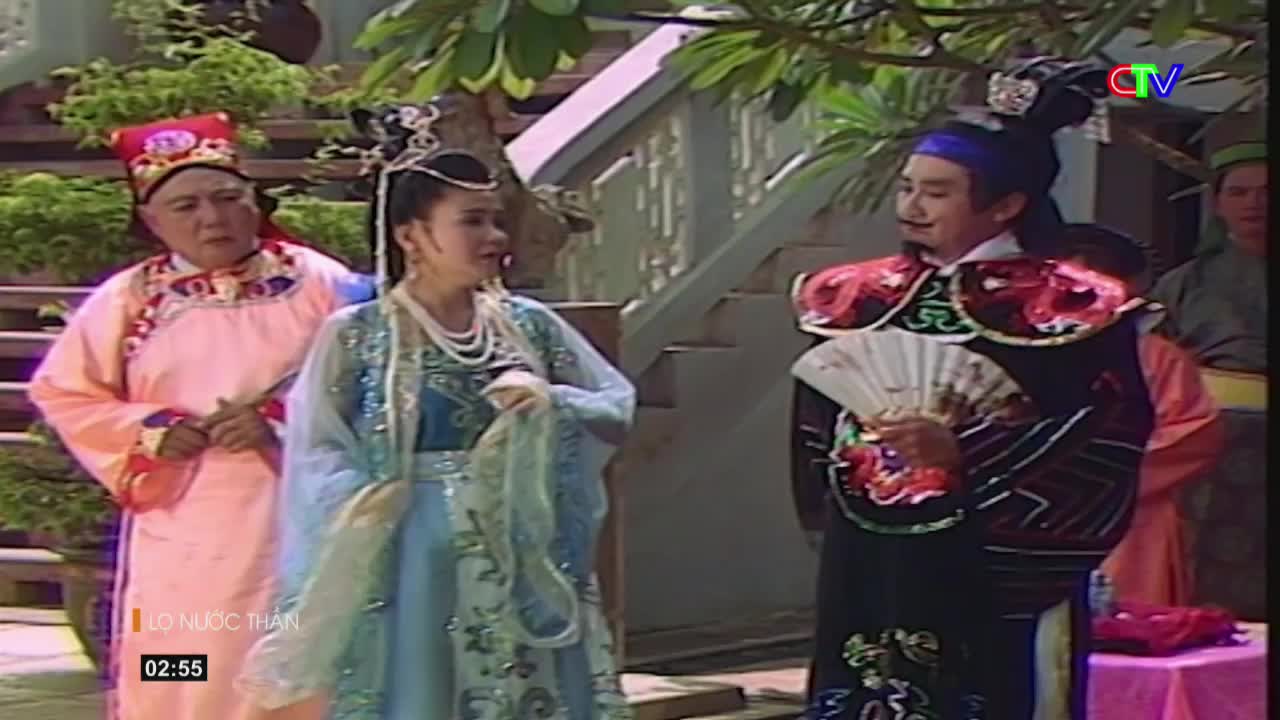 A woman in a flowing blue gown and a man in a dark robe holding a fan stand facing each other. Another man in a pink robe and a tall hat watches from the left.