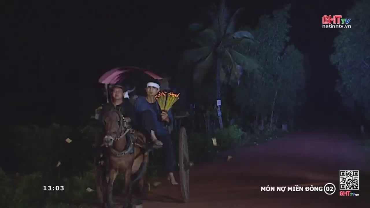 A horse-drawn cart, lit by the dark, moves down a road, the occupants under a pink umbrella. One man clutches a bundle of lit sticks, likely incense, as they pass through the night.
