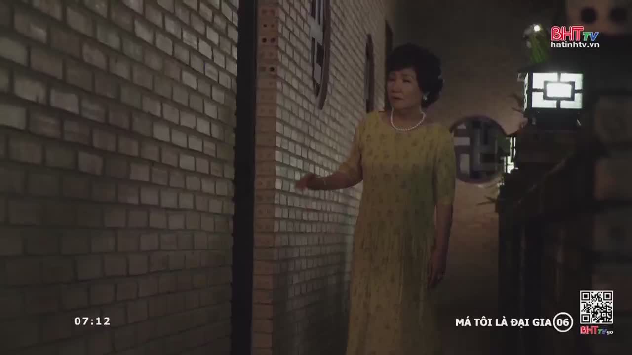 A woman in a yellow dress walks along a brick wall, her hand outstretched. The scene, broadcast by Ha Tinh TV, is set in a dimly lit alleyway.
