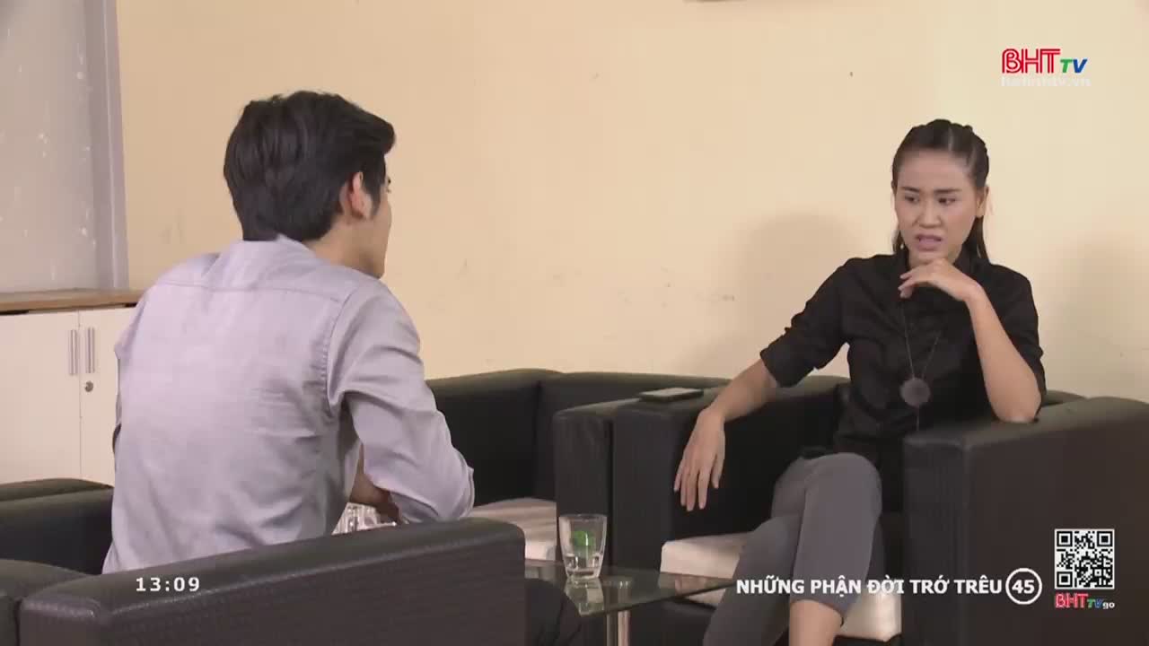 A woman in a black shirt gestures with her hand, her expression a mix of concern and frustration. Across from her, a man in a light gray shirt listens intently, the scene unfolding on Ha Tinh TV.
