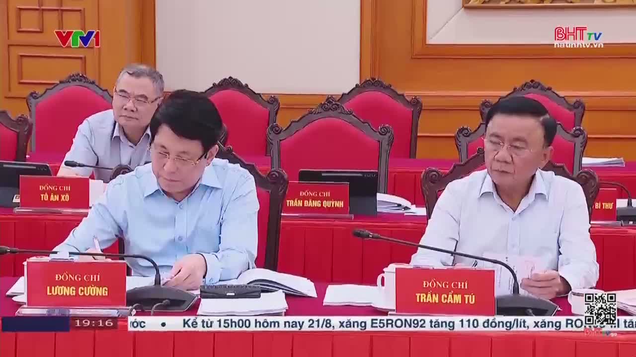 Men in light-colored shirts sit at a long, red-covered table, microphones in front of them. A Ha Tinh TV logo is visible in the corner, and text at the bottom of the screen mentions a fuel price increase.
