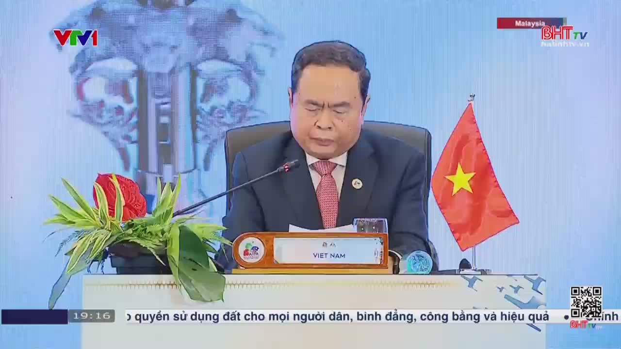 A man in a suit, seated behind a desk with a "VIET NAM" placard, reads intently. The Vietnamese flag stands to his right, while Ha Tinh TV's logo is visible in the corner.

