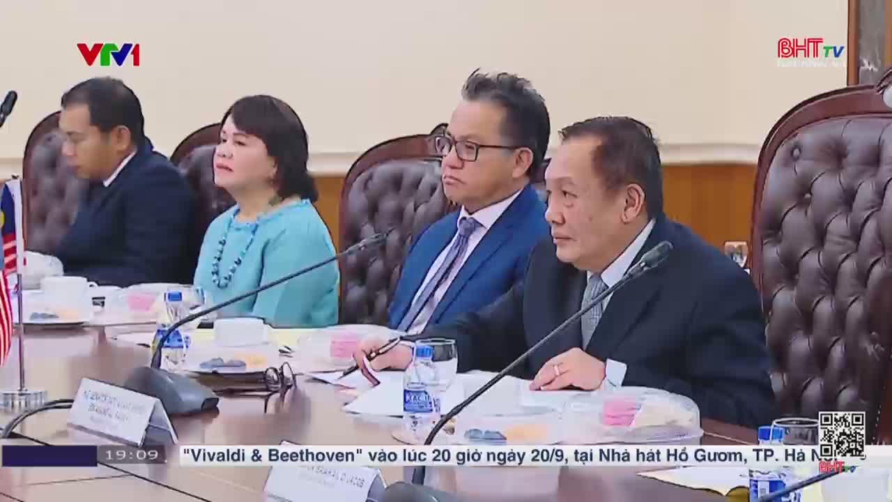A group of people in suits and business attire are seated around a large table, listening intently. The broadcast from Ha Tinh TV on VTV1, Vietnam, indicates a performance of "Vivaldi & Beethoven" is coming up.
