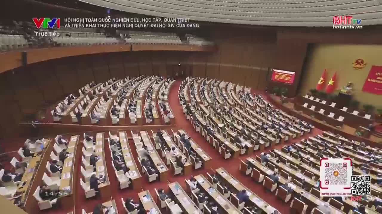The vast hall is filled with rows of delegates, each seated at their own desk. A large screen displays text, and two Vietnamese flags stand prominently at the front.