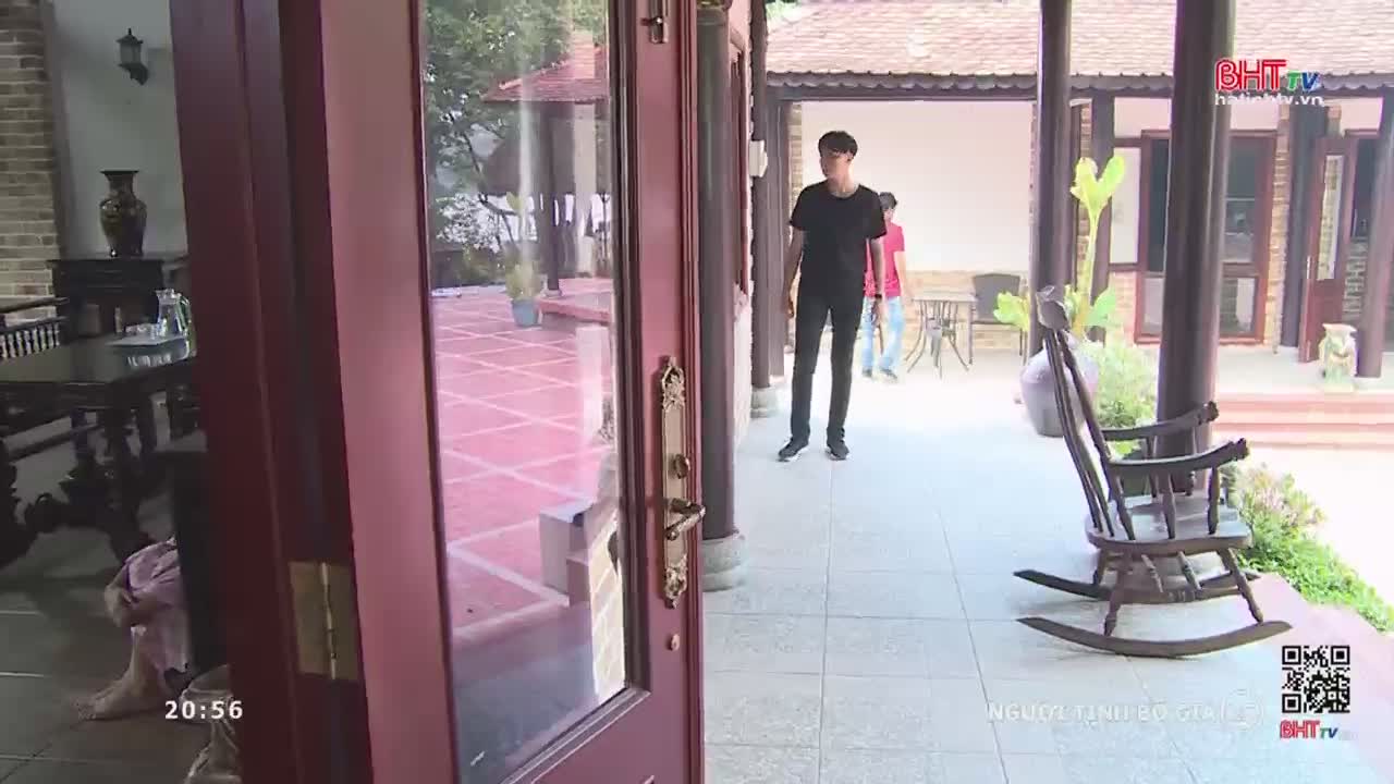 A young man in a black t-shirt walks across a tiled courtyard. A rocking chair sits empty on the porch.