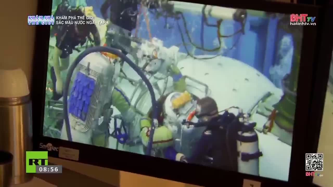 Two divers in bulky suits work near a large, white, spherical object. The scene, broadcast on Ha Tinh TV, shows them tethered to a complex structure.