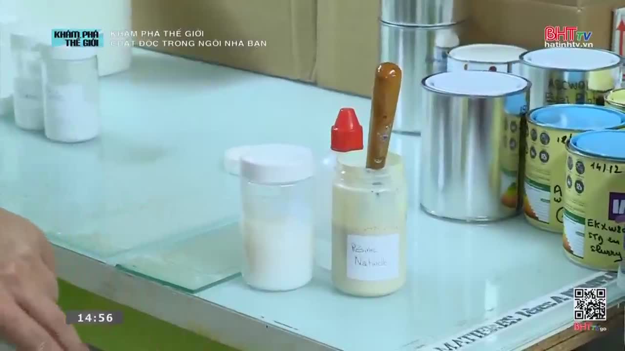 A wooden-handled brush rests in a jar of light-colored paste. Nearby, several metal cans with colorful labels are lined up on a counter.