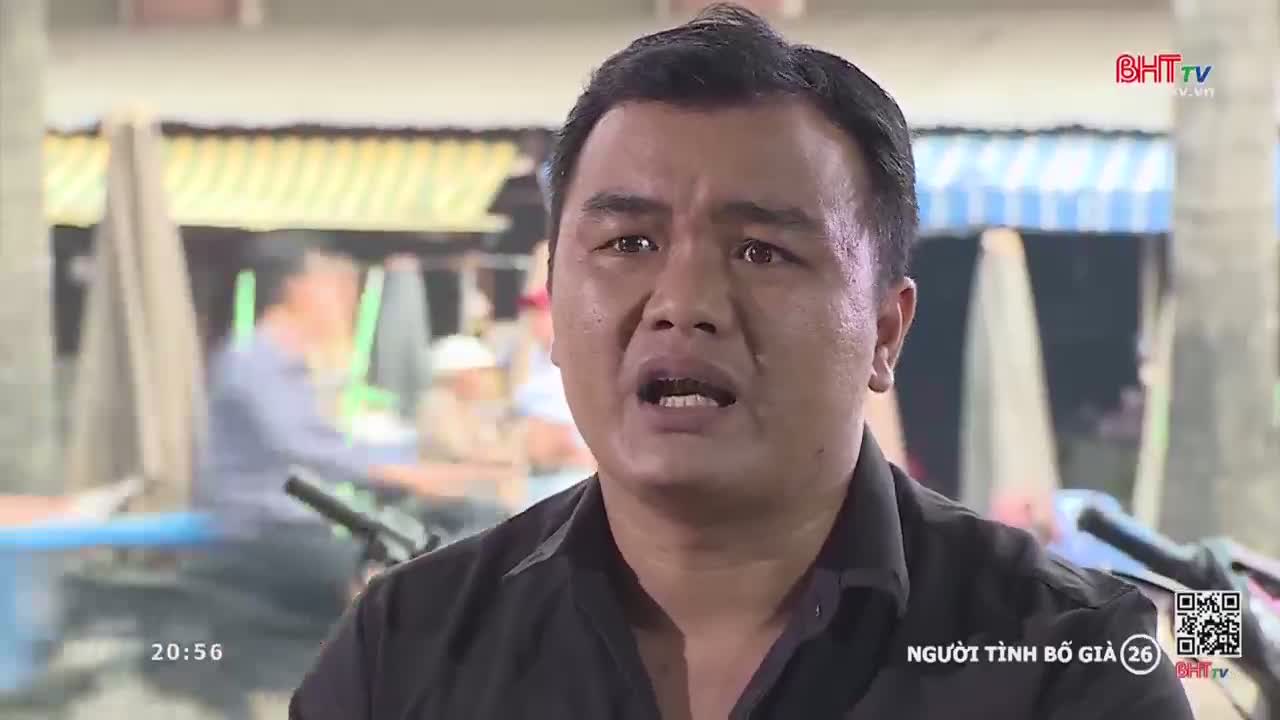 A man with a distressed expression speaks directly to the camera, his mouth open. Behind him, a bustling market scene unfolds with blurred figures and stalls under a striped awning.