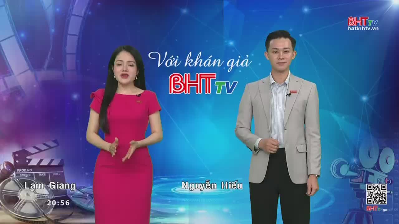 A woman in a bright pink dress stands to the left, her hands gesturing as she speaks. Beside her, a man in a light grey suit stands attentively, his gaze directed forward.