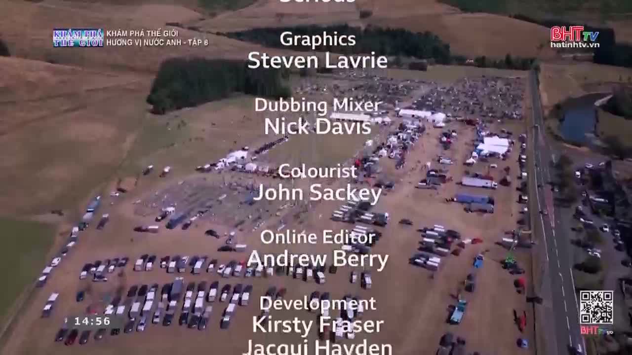 Cars are parked in rows across a wide, open field. Tents and people are scattered throughout the area, with a road running alongside.