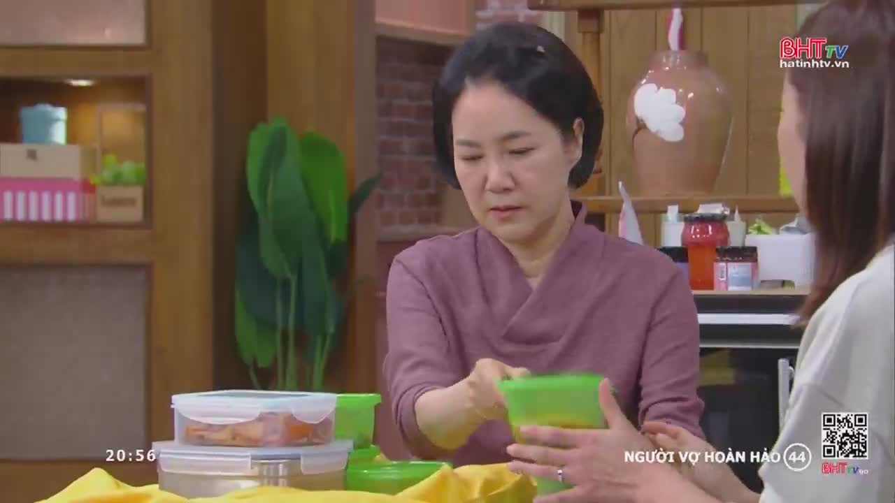 A woman in a purple shirt hands a green container to another woman. The scene appears to be from a Vietnamese television program, possibly a drama, given the on-screen text.