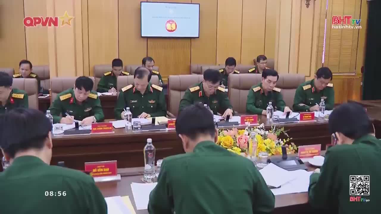 Men in military uniforms sit at a long table, intently focused on documents and taking notes. A screen displays a symbol, and the Ha Tinh TV logo is visible in the corner.