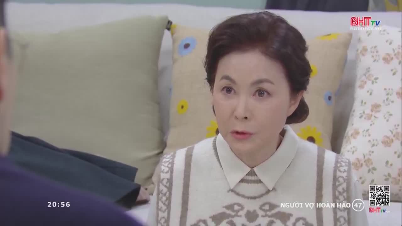 A woman with dark hair, wearing a patterned sweater, speaks with a serious expression. She sits on a couch with decorative pillows behind her, as a BHT TV logo appears in the corner.