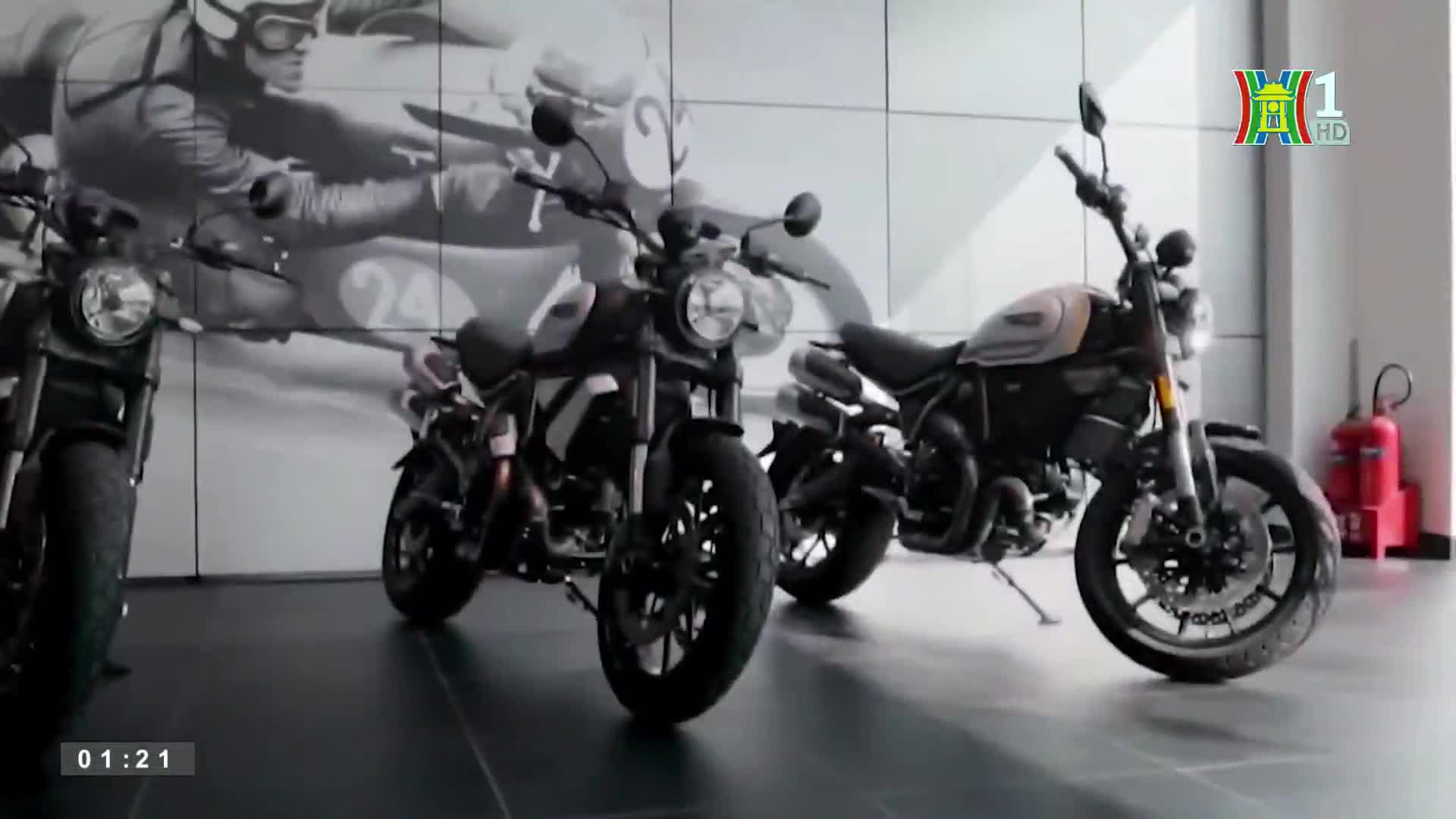 Three motorcycles are parked on a glossy floor, their round headlights reflecting the showroom lights. The HanoiTV1 logo sits in the corner, and the time is 01:21.
