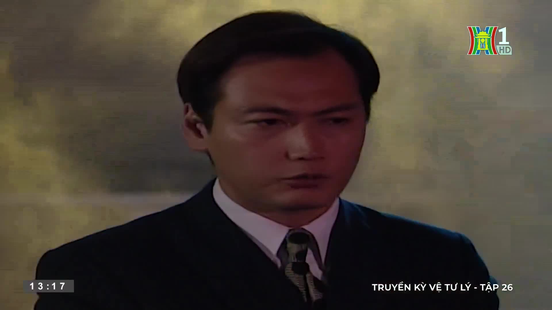 A man in a dark suit stares intently, his gaze fixed on something out of frame. The HanoiTV1 logo and Vietnamese text indicate a scene from a television show.
