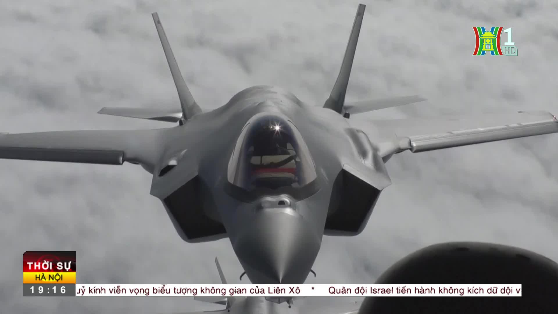 A gray jet, its nose pointed directly at me, cuts through the overcast sky. The HanoiTV1 logo and Vietnamese text are visible in the lower corners of the screen.
