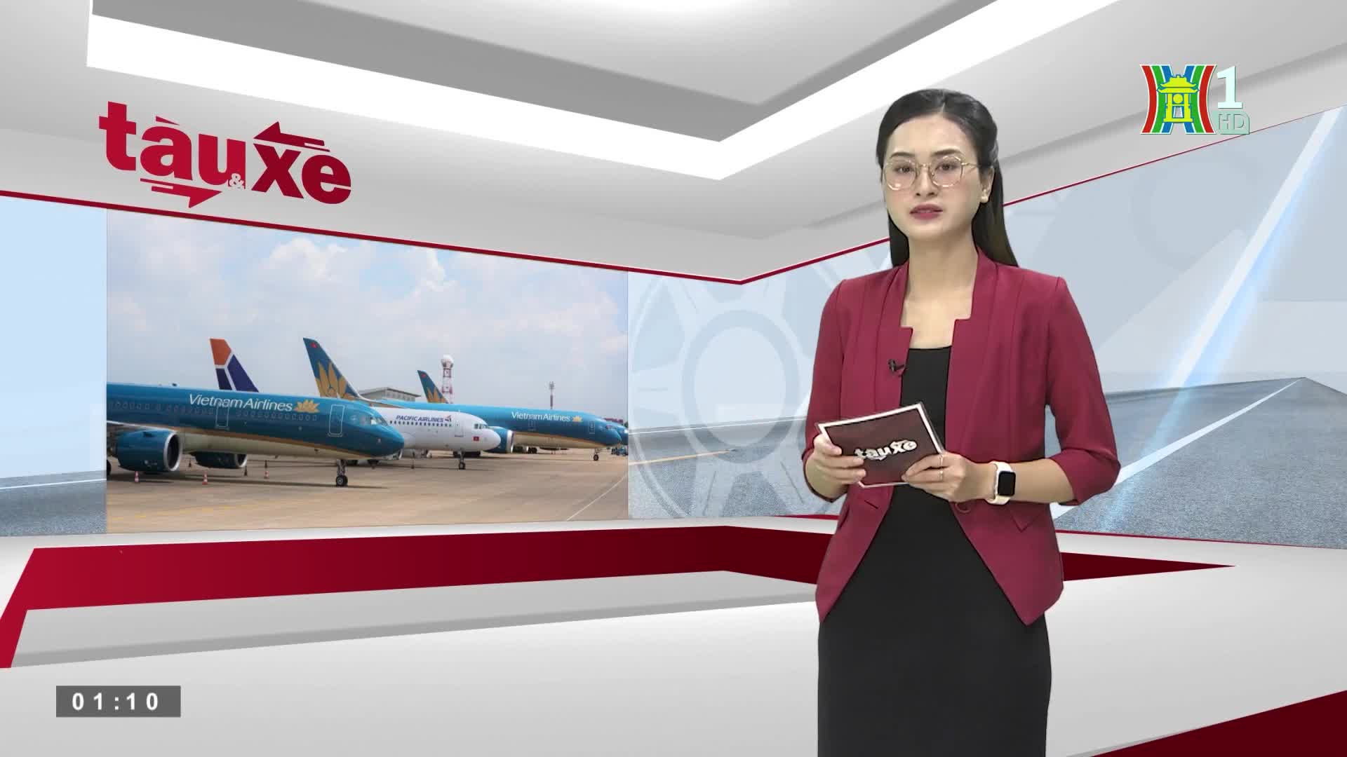 A woman in a maroon jacket and glasses stands in a studio, holding a small sign. Behind her, a screen shows several Vietnam Airlines planes parked on a tarmac.
