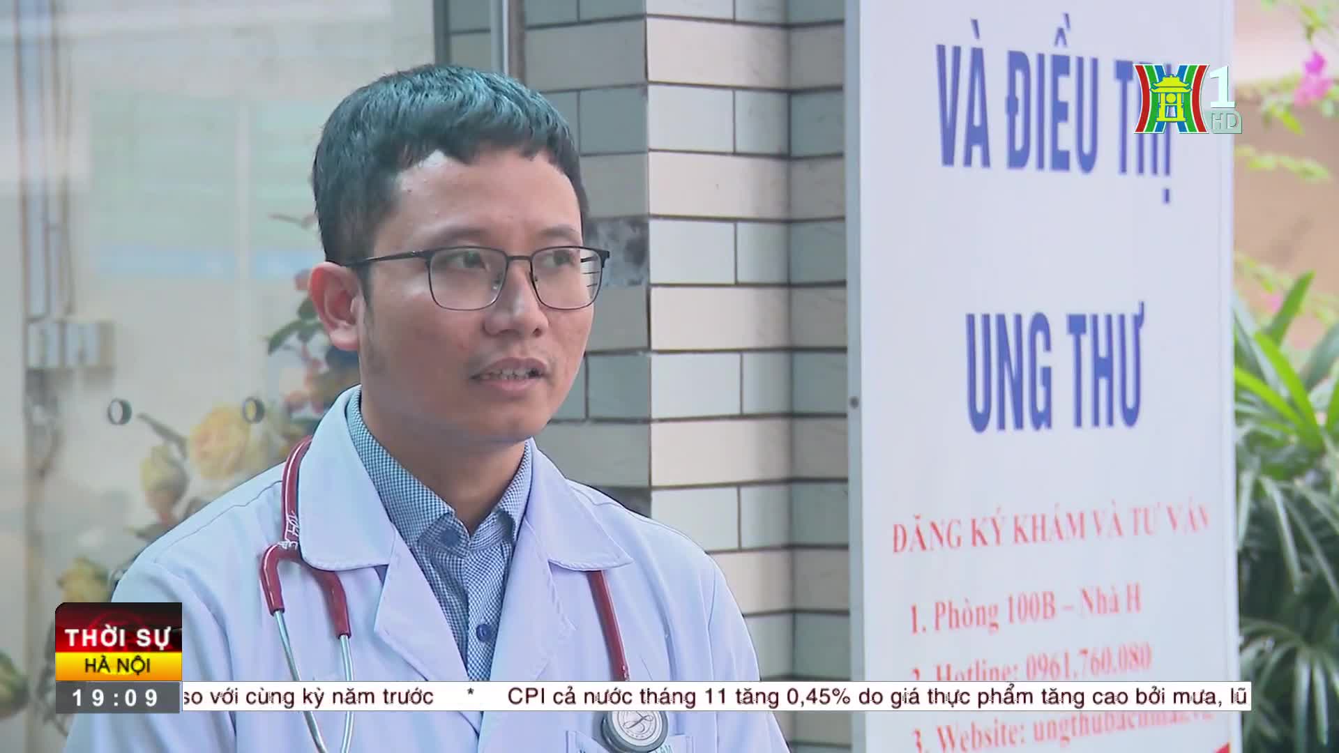 A doctor in a white coat and glasses is speaking, a stethoscope around his neck. HanoiTV1's logo is in the corner, and a sign about cancer treatment is visible behind him.
