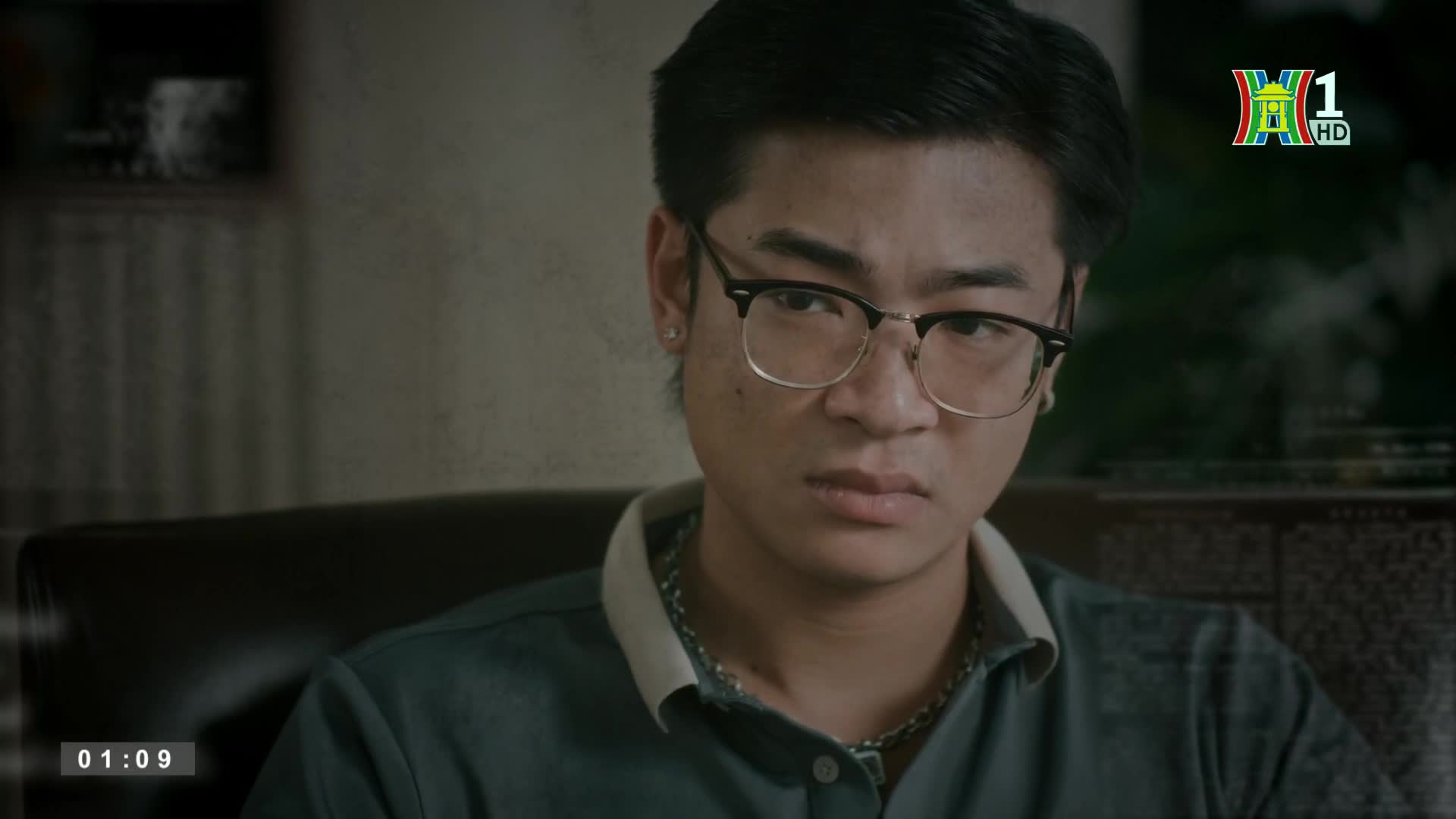 A young man with glasses stares directly ahead, his expression unreadable. The HanoiTV1 logo in the corner confirms this is a scene from a Vietnamese broadcast.
