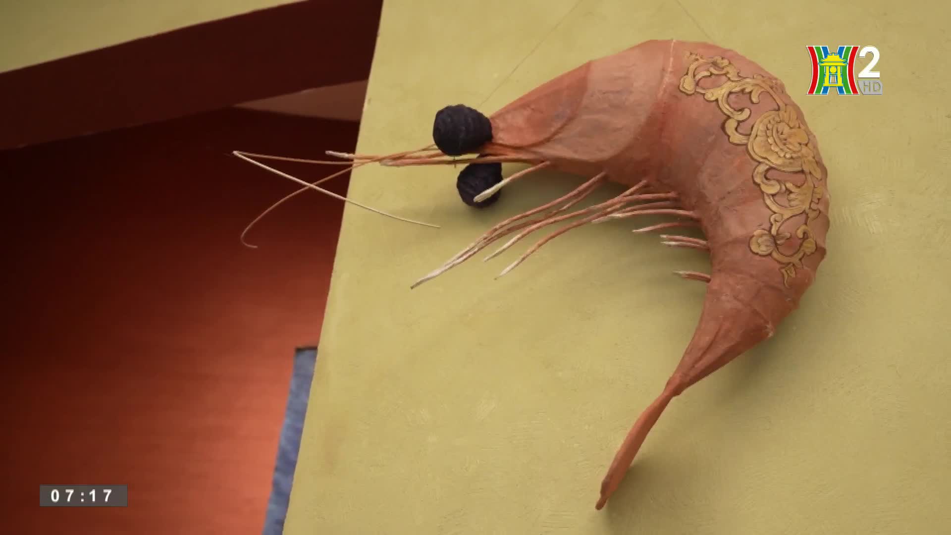 A large, paper shrimp hangs on the wall, its body curved and decorated with gold patterns. The HanoiTV2 logo sits in the corner, and the time is 07:17.

