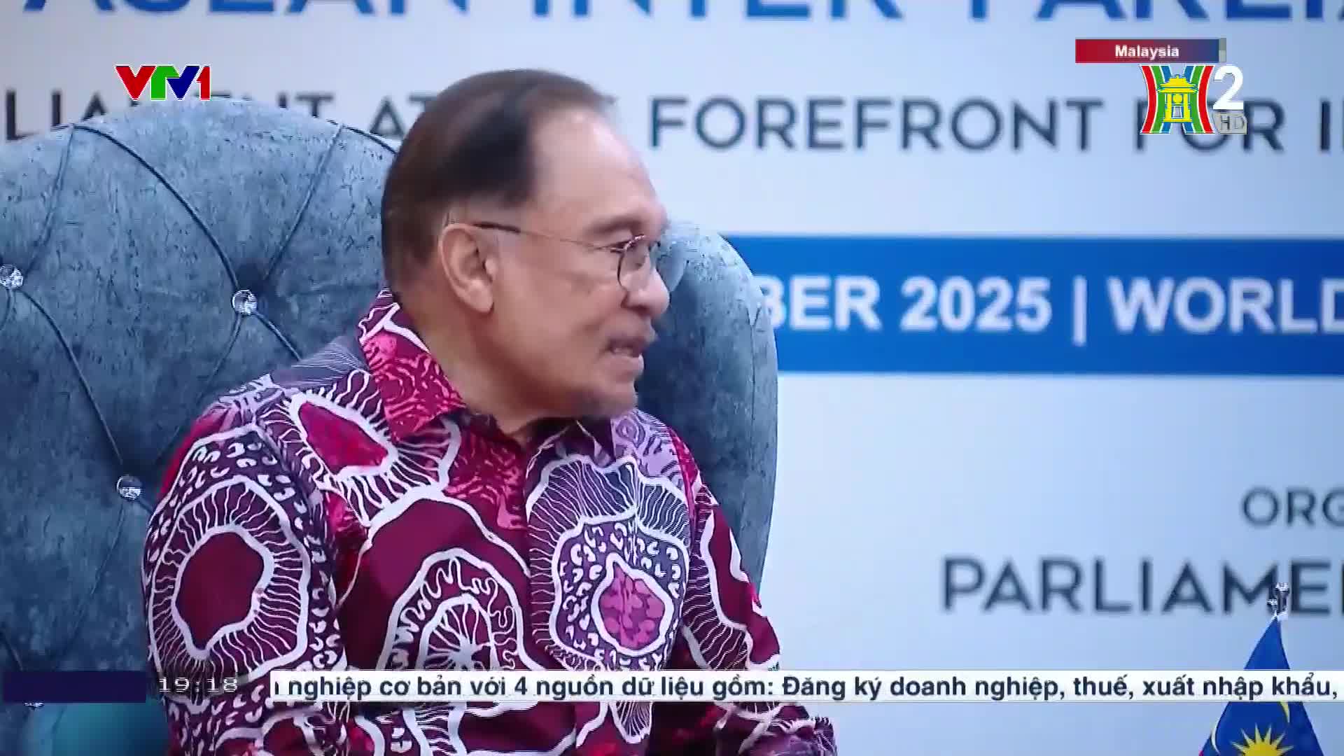 A man in a patterned shirt speaks, his mouth moving as he gestures with his hands. The HanoiTV2 logo is visible in the corner, and the backdrop mentions "Malaysia."
