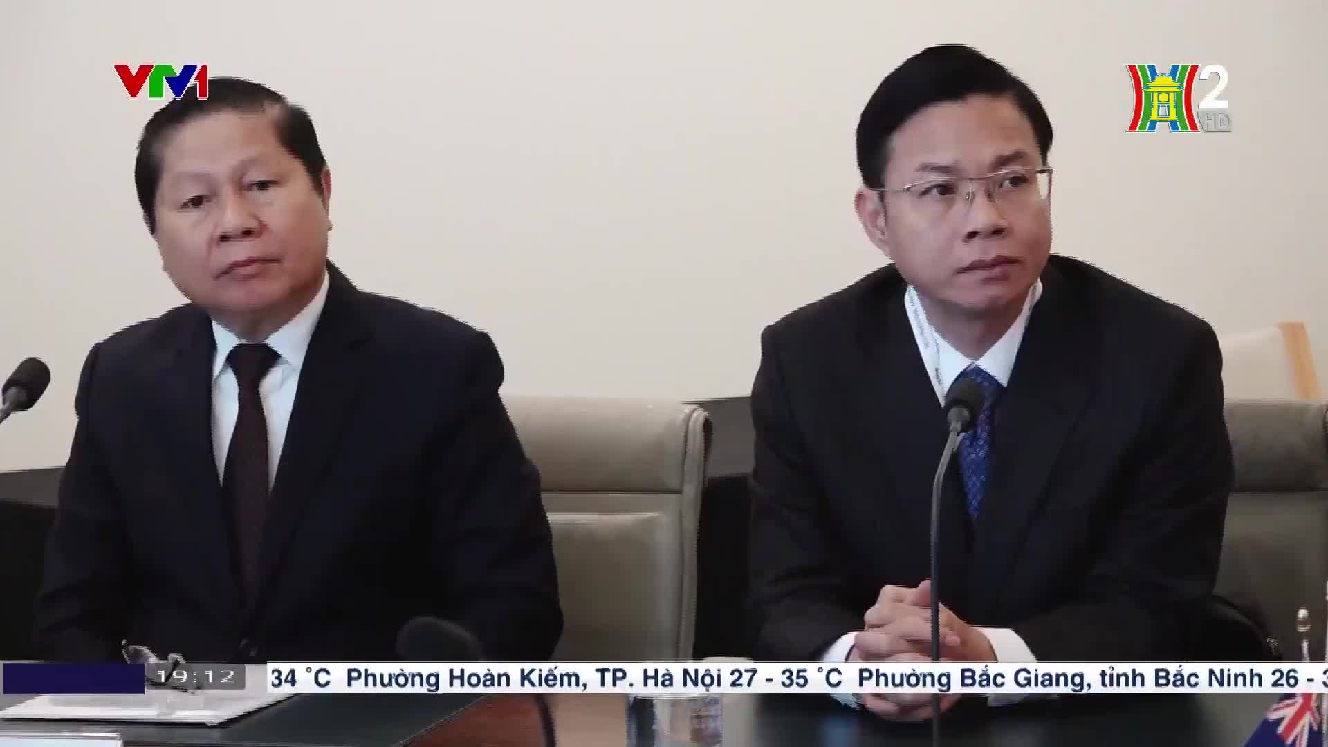 Two men in dark suits sit behind a table, facing forward with serious expressions. The HanoiTV2 logo is visible in the corner, and the VTV1 logo is at the top left.
