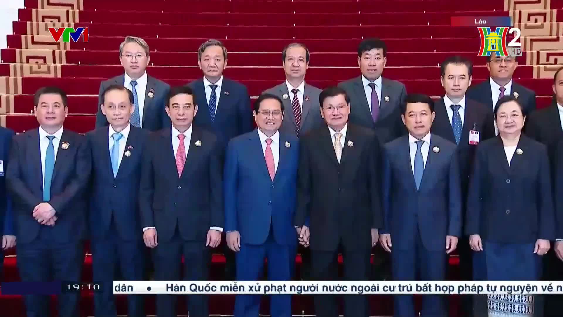 A group of men and one woman in suits stand on a red carpeted staircase, posing for a photo. The HanoiTV2 logo is visible in the corner, and the time is displayed at the bottom of the screen.
