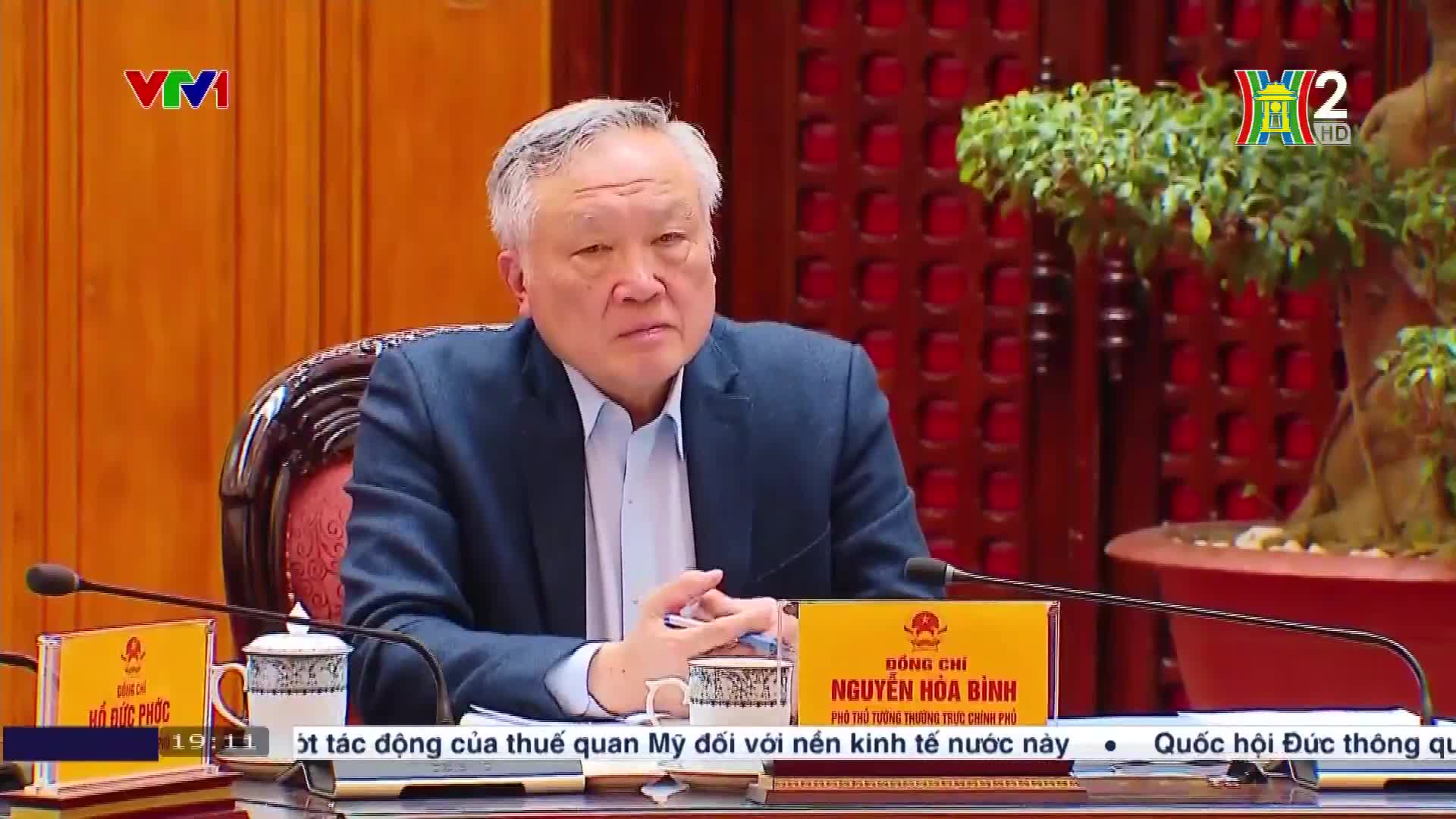 A man in a blue suit sits at a table, looking directly at the camera. The HanoiTV2 logo is visible in the corner, and a nameplate identifies him as Nguyen Hoa Binh.
