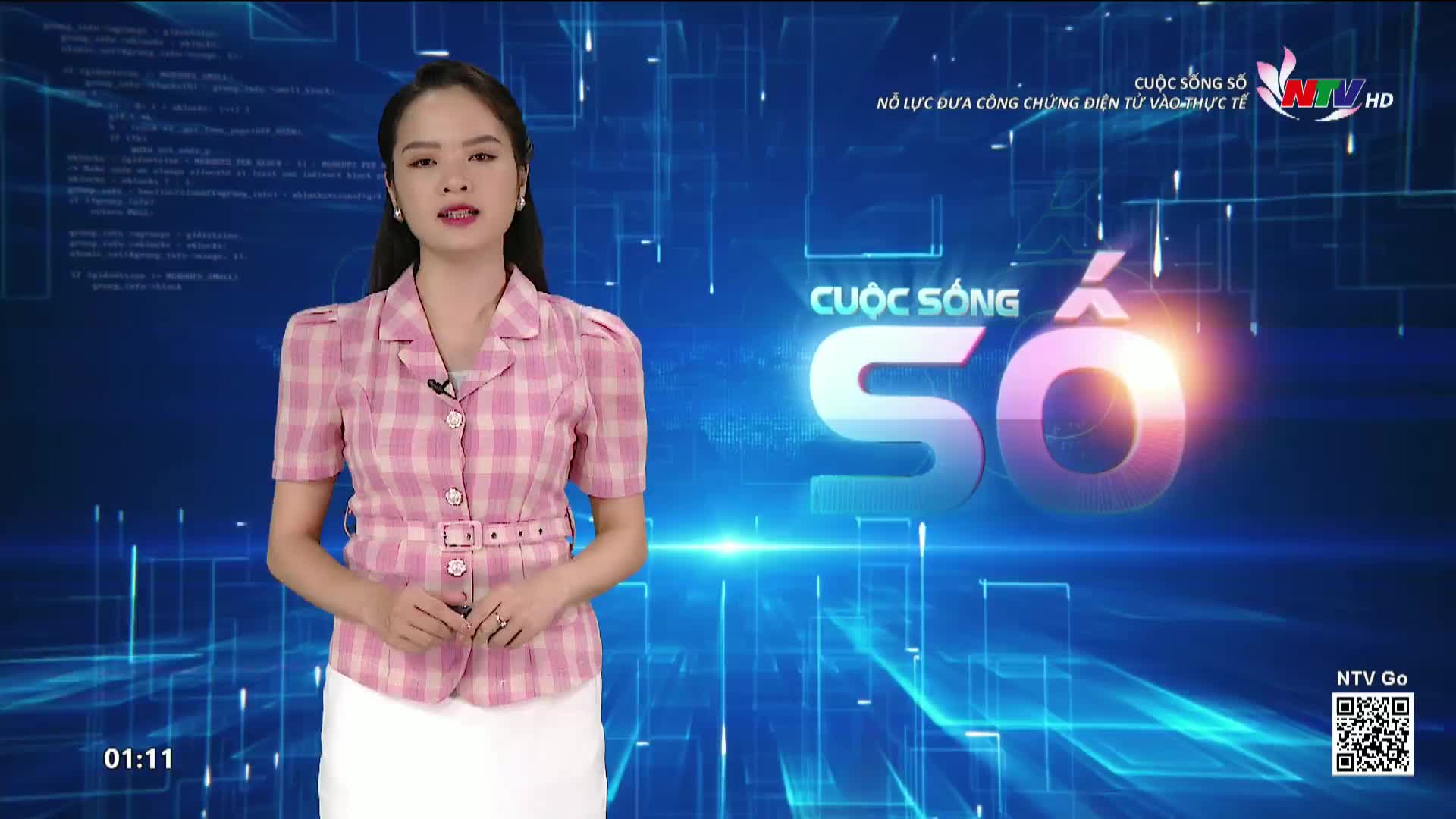 A woman in a pink plaid jacket stands in front of a blue background, speaking directly to the camera. The Nghe An TV logo is visible, along with Vietnamese text and graphics.
